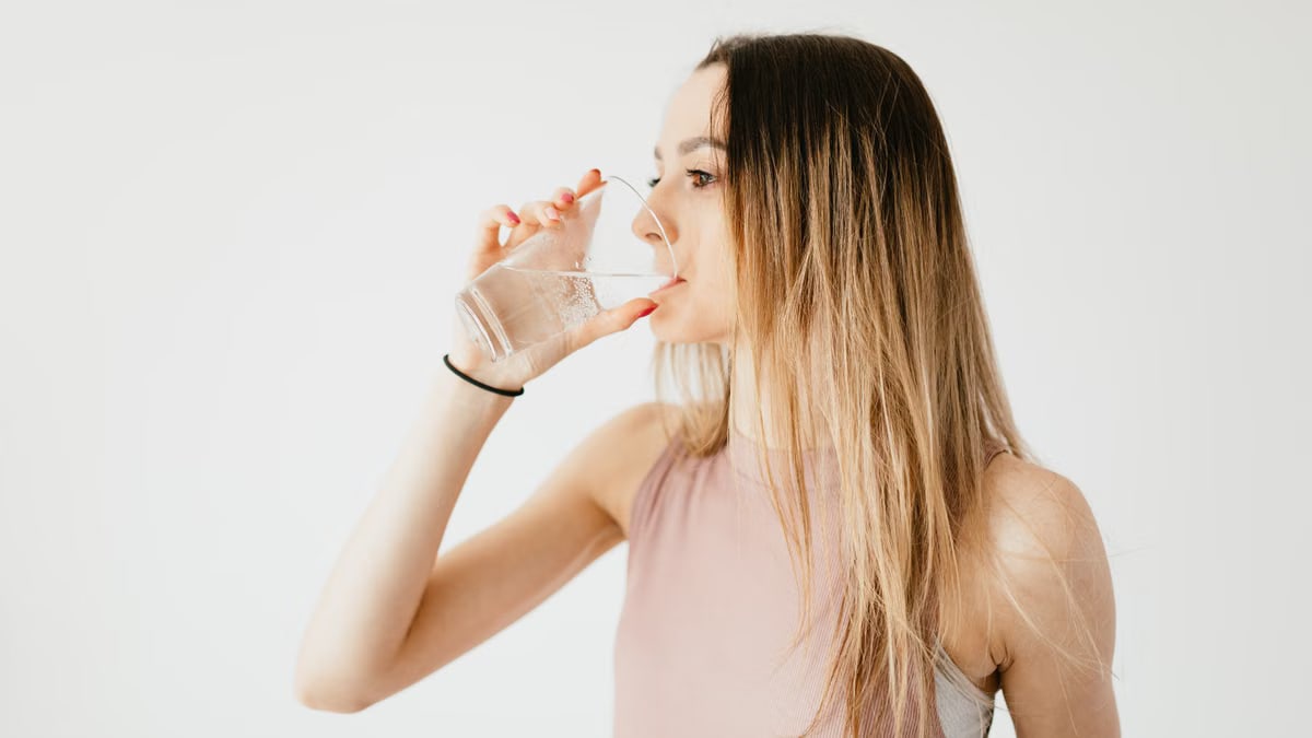 Young thirsty fit female with long hair in sportswear drinking water while recreating after workout