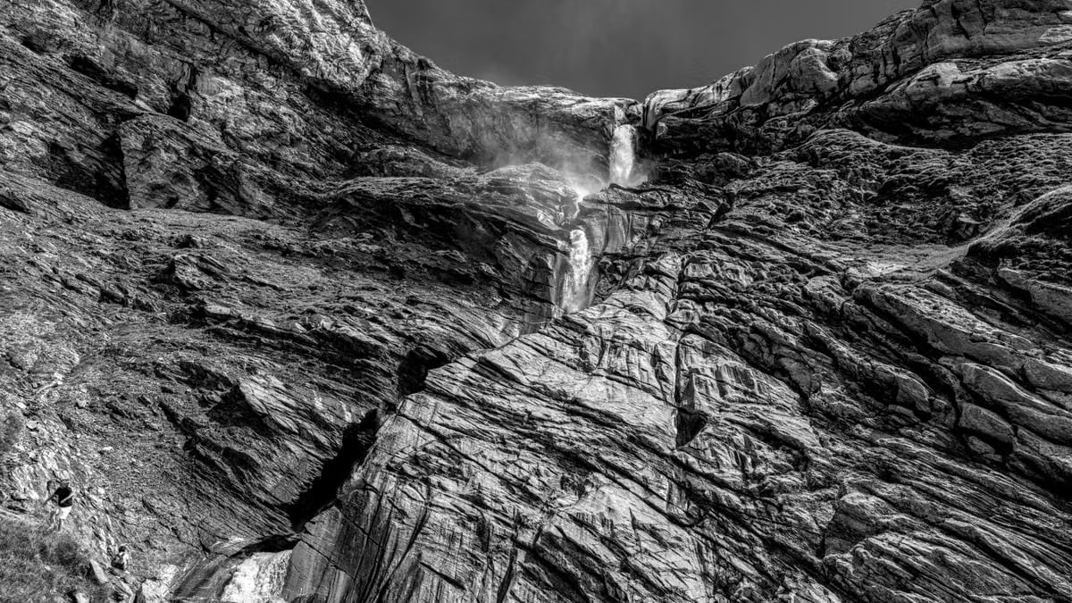 A stunning black and white capture of a waterfall flowing down rugged rock formations in a mountainous landscape.
